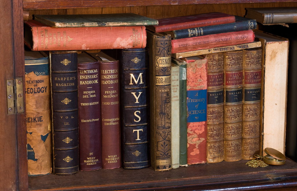 A bookshelf filled with science, engineering & fantasy books with the Myst book in the middle