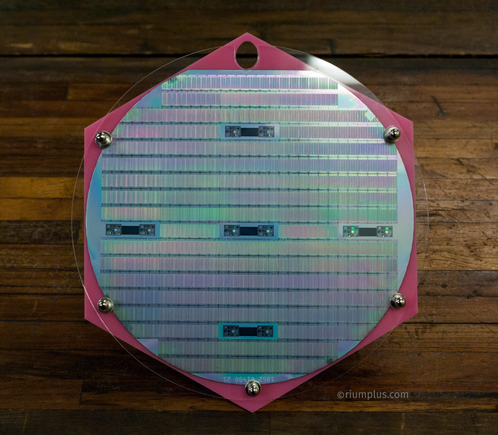 A Silicon Wafer in a custom pink Acrylic holder. It shines pink and green in the light. Engraved on it are hundreds of SRAM memory chips