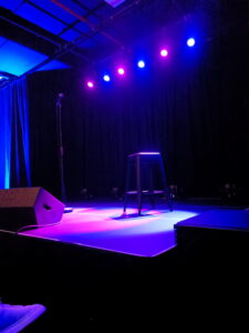A standup comedy stage lit by blue and purple light